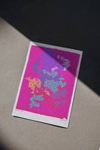 Colorful abstract design on a pink background with a white border, placed on a textured surface.