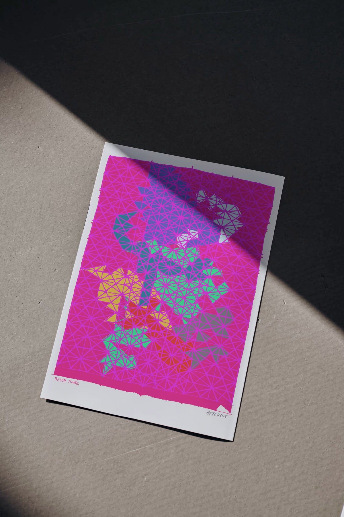 Colorful abstract design on a pink background with a white border, placed on a textured surface.