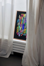Colorful abstract art on a blackboard framed in a wooden border, hanging on a wall with white curtains.